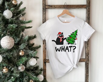 May include: White t-shirt with a black cat wearing a Santa hat and pulling down a Christmas tree. The text "WHAT?" is printed below the image.