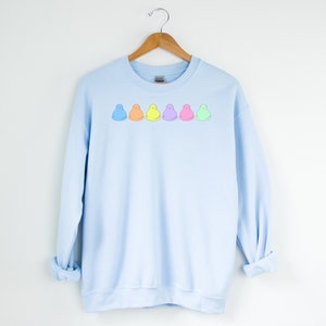 Peut inclure: Sweat-shirt bleu clair avec une rang&eacute;e de six guimauves de dessin anim&eacute; color&eacute;es imprim&eacute;es sur le devant.