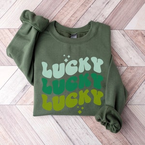 May include: A green sweatshirt with the word "LUCKY" printed three times in a retro font, with each word in a different shade of green.