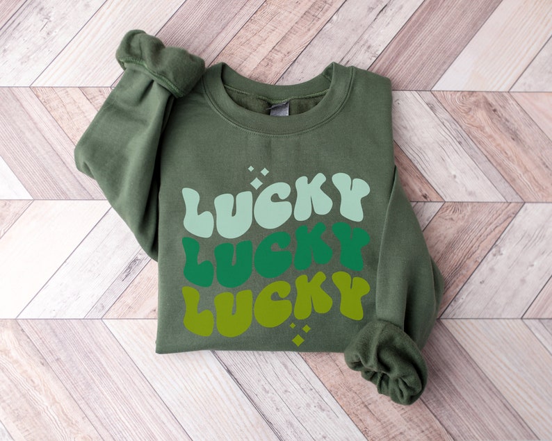 May include: A green sweatshirt with the word "LUCKY" printed three times in a retro font, with each word in a different shade of green.