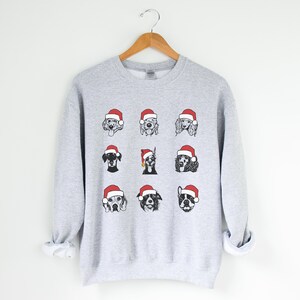 May include: A gray sweatshirt with a Christmas-themed design featuring nine different dog breeds wearing Santa hats. The dogs are illustrated in black and white.