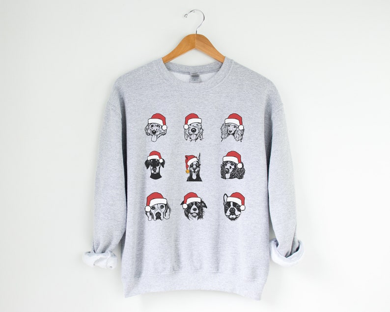 May include: A gray sweatshirt with a Christmas-themed design featuring nine different dog breeds wearing Santa hats. The dogs are illustrated in black and white.