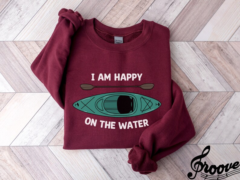 May include: Burgundy sweatshirt with the text "I am happy on the water" and a green kayak with a paddle.