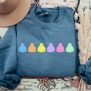 Peut inclure: Un sweat-shirt bleu sarcelle avec une rang&eacute;e de cinq guimauves en forme de poussins pastel imprim&eacute;es sur le devant.