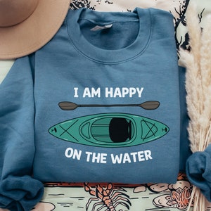 May include: A blue sweatshirt with the text "I am happy on the water" and a cartoon image of a green kayak with a paddle.