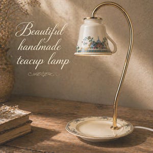 May include: A handmade teacup lamp with a gold-colored curved stand. The teacup lamp is white with floral designs and sits on a matching saucer. The text "Beautiful handmade teacup lamp" is displayed on the image.