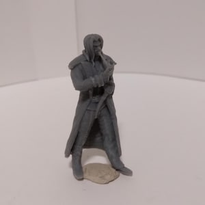 May include: A gray plastic miniature figurine of a person wearing a long coat and holding a staff. The figurine is standing on a small gray rock.