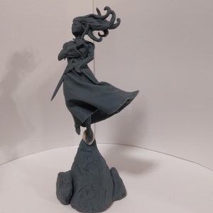 May include: A gray 3D printed figurine of a woman with flowing hair, holding a sword and standing on a rock base.