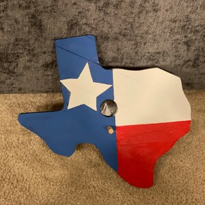 May include: A wooden cutout of the state of Texas painted in the colors of the American flag. The star is white, the top portion is blue, and the bottom portion is red.
