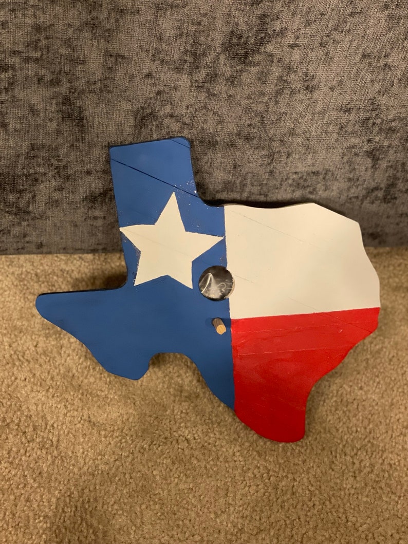 May include: A wooden cutout of the state of Texas painted in the colors of the American flag. The star is white, the top portion is blue, and the bottom portion is red.