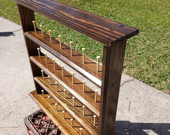May include: A dark brown stained wooden display rack featuring four horizontal shelves. Each shelf is equipped with multiple small, light-colored wooden golf tees inserted into pre-drilled holes, arranged in rows for organizing or showcasing golf accessories.