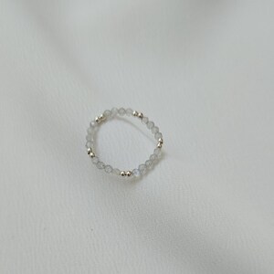May include: A delicate ring made of small, clear, iridescent beads with silver and gold accents.