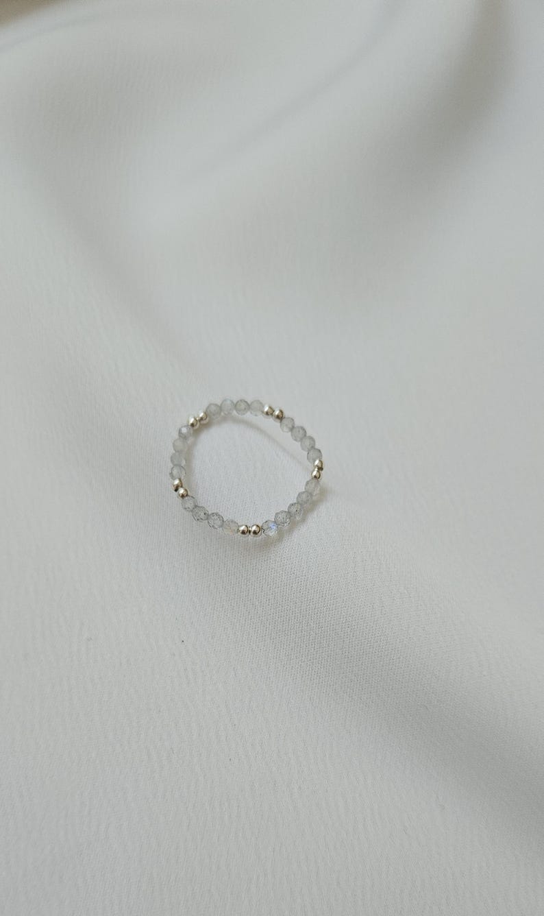 May include: A delicate ring made of small, clear, iridescent beads with silver and gold accents.