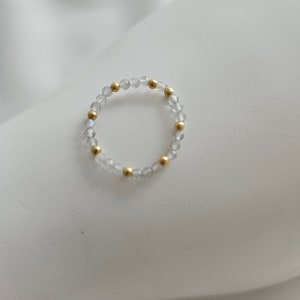 May include: A delicate ring made of clear beads and gold accents. The ring is simple and elegant, perfect for everyday wear.