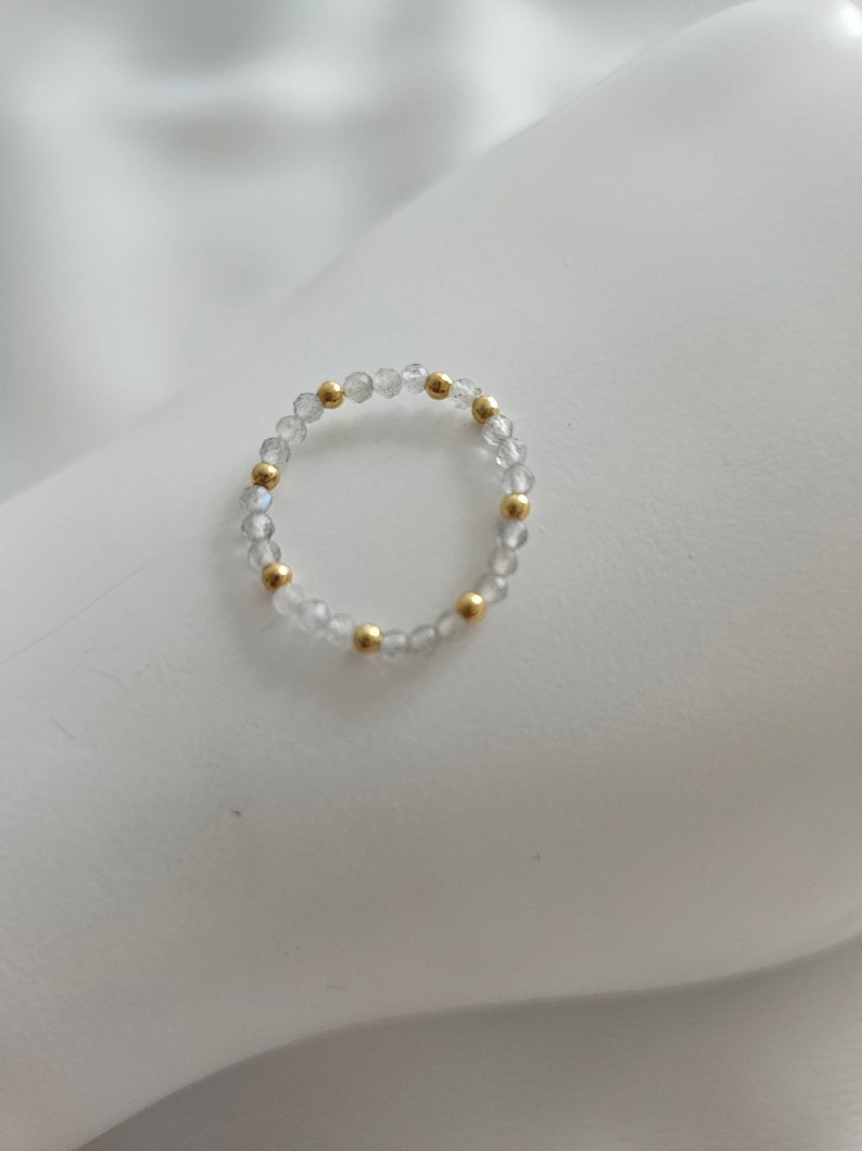May include: A delicate ring made of clear beads and gold accents. The ring is simple and elegant, perfect for everyday wear.