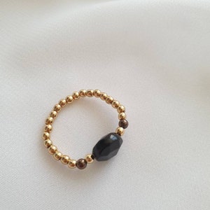 May include: A gold beaded ring with a black gemstone. The ring is made of small gold beads and has a single black gemstone in the center.