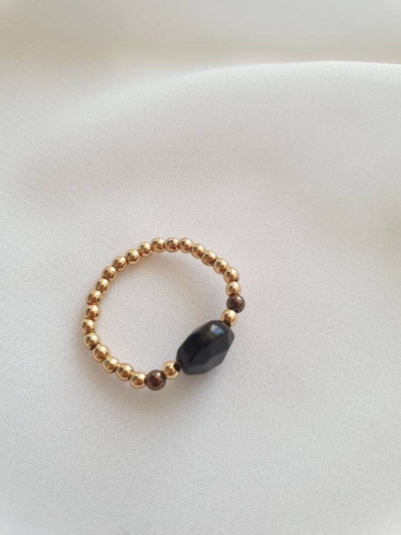 May include: A gold beaded ring with a black gemstone. The ring is made of small gold beads and has a single black gemstone in the center.