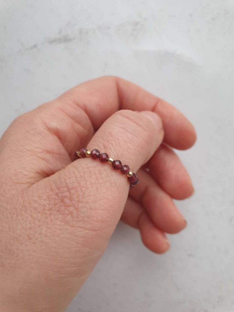 May include: A ring made of small, dark red beads with gold accents.