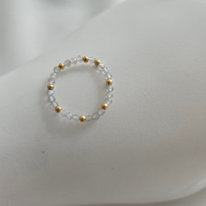 May include: A delicate ring made of small, clear beads with gold accents. The ring is simple and elegant.