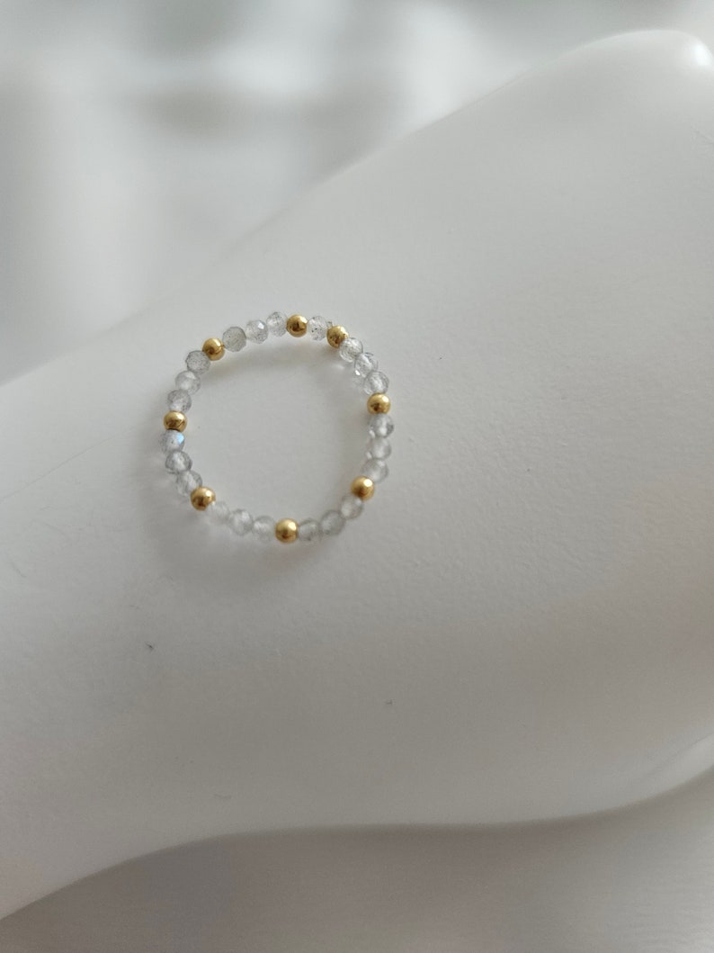 May include: A delicate ring made of small, clear beads with gold accents. The ring is simple and elegant.