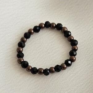 K&ouml;nnte beinhalten: Ein Armband aus schwarzen und braunen Perlen mit abwechselnd schwarzen und braunen Perlen.