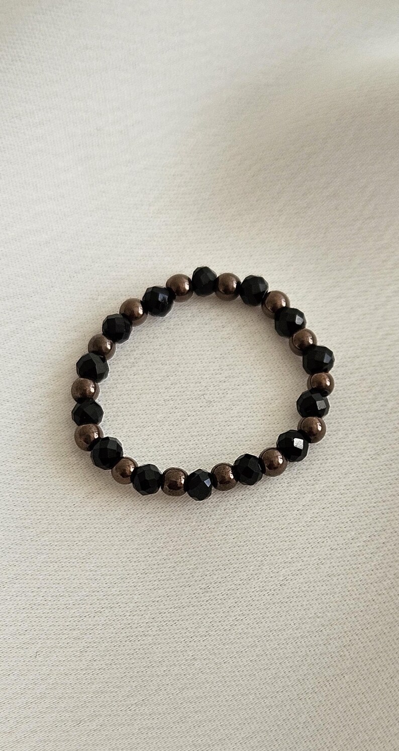 K&ouml;nnte beinhalten: Ein Armband aus schwarzen und braunen Perlen mit abwechselnd schwarzen und braunen Perlen.
