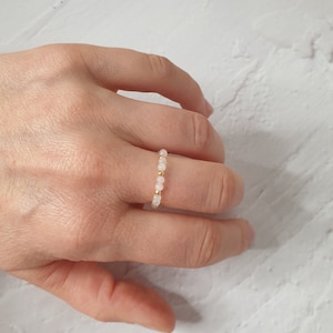 May include: A delicate ring made of small pink beads and gold spacers. The ring is worn on a finger.