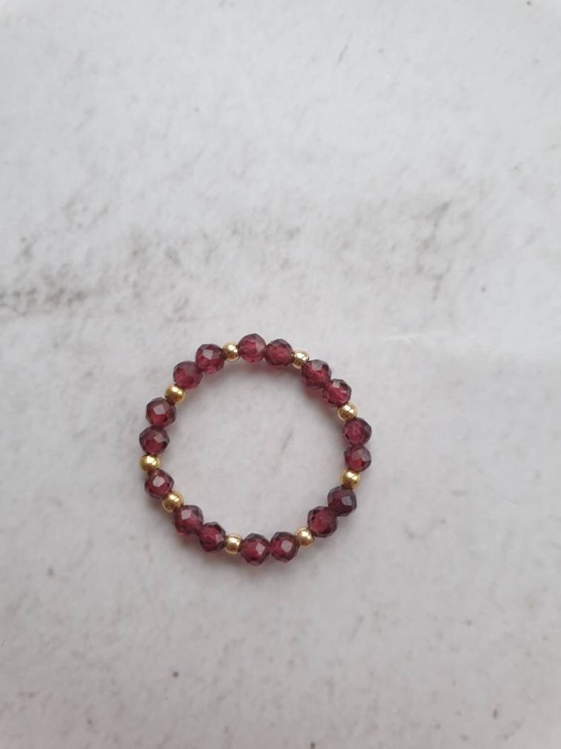 May include: A ring made of small, dark red beads with gold accents.