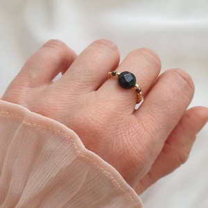 May include: A gold ring with a black gemstone bead. The ring is made of small gold beads.