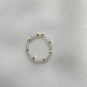 May include: A delicate bracelet made of clear and iridescent beads with gold accents.