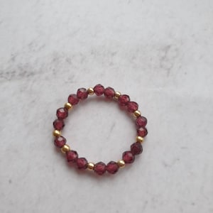 May include: A gold ring with a band of small, dark red beads.