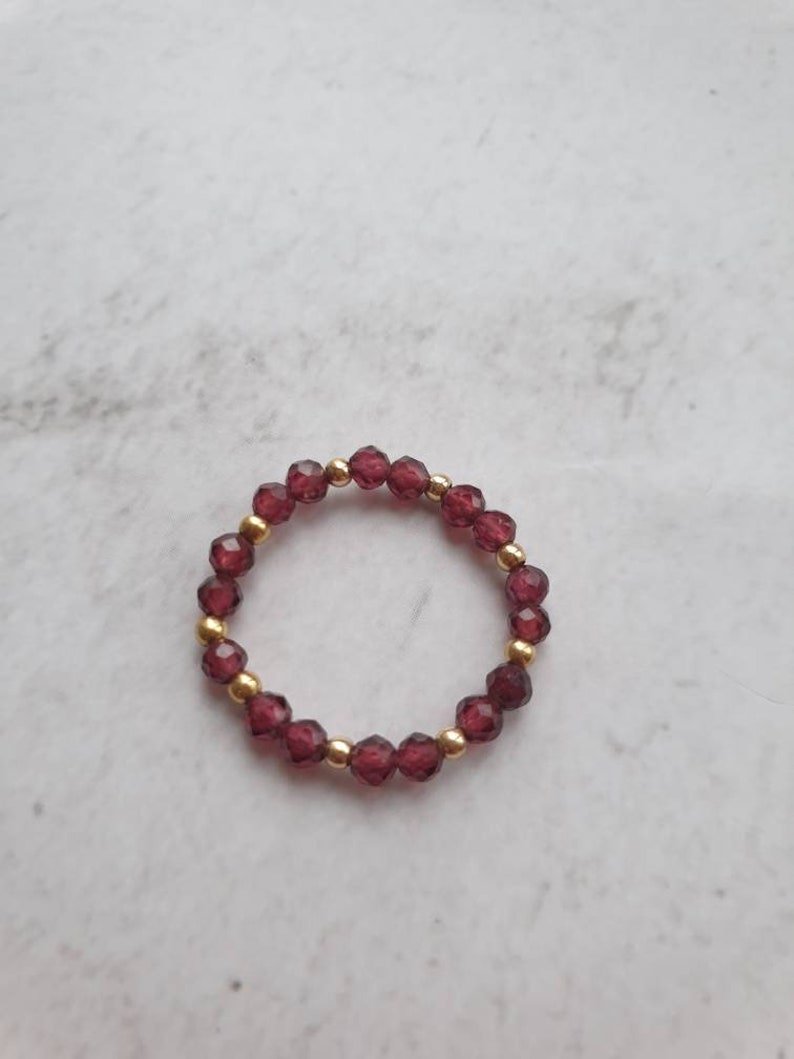 May include: A gold ring with a band of small, dark red beads.