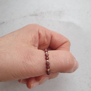 May include: A gold and garnet beaded ring worn on a finger.