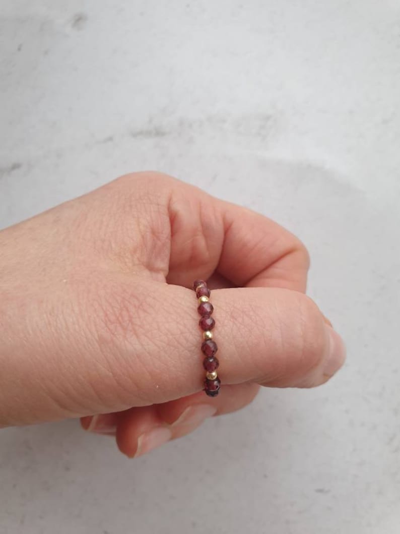 May include: A gold and garnet beaded ring worn on a finger.