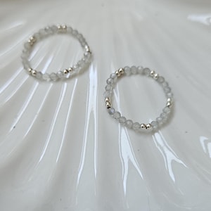 May include: Two silver rings with white gemstone beads on a white ceramic plate with a gold rim.