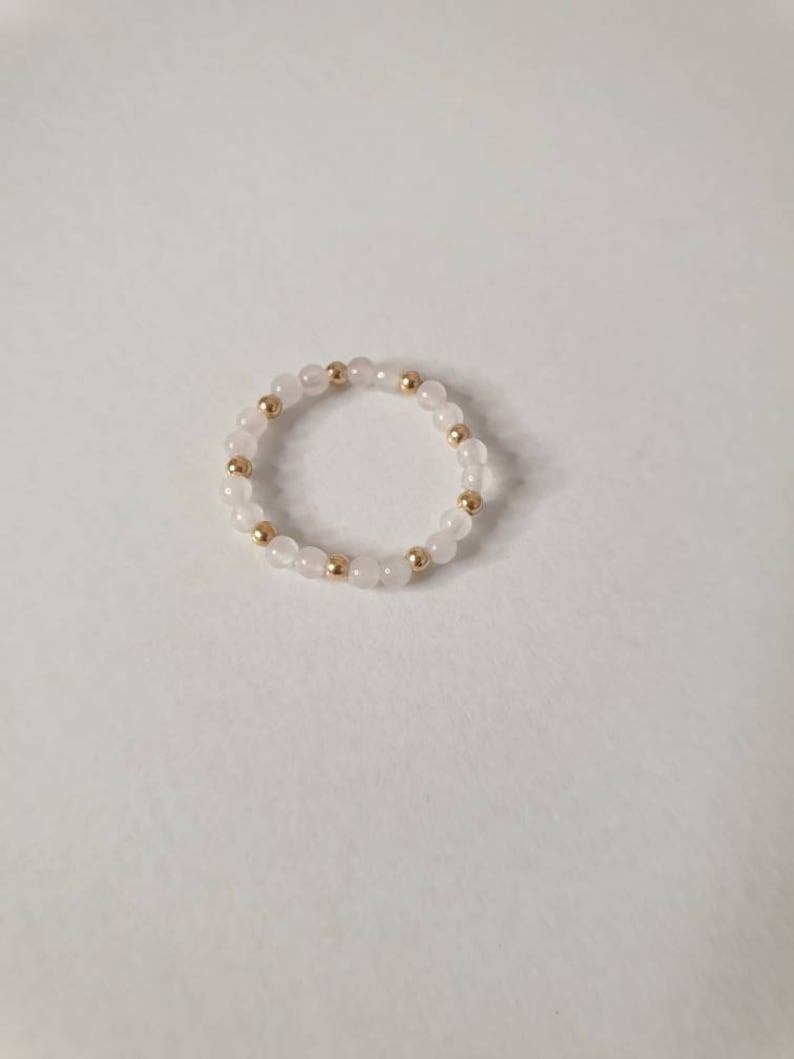 May include: A delicate ring made of small white beads and gold beads.