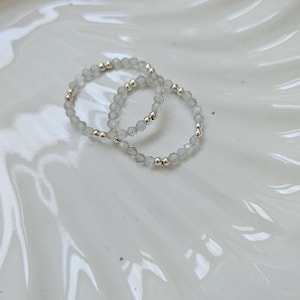 May include: Two silver beaded bracelets with clear faceted stones. The bracelets are on a white ceramic plate with a gold rim.