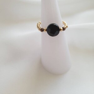 May include: A gold beaded ring with a black round stone in the center.