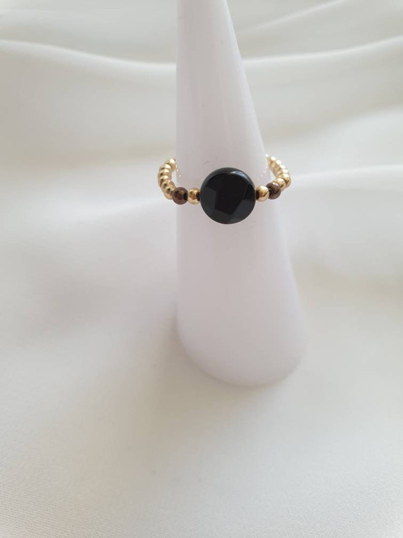 May include: A gold beaded ring with a black round stone in the center.