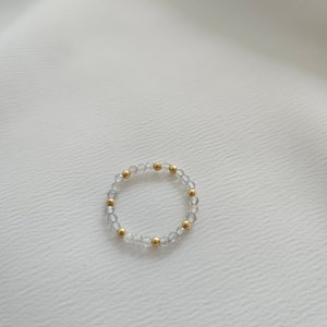 May include: A delicate bracelet made of clear and gold beads. The bracelet is made of small, round beads that are strung together on a thin, clear elastic cord.