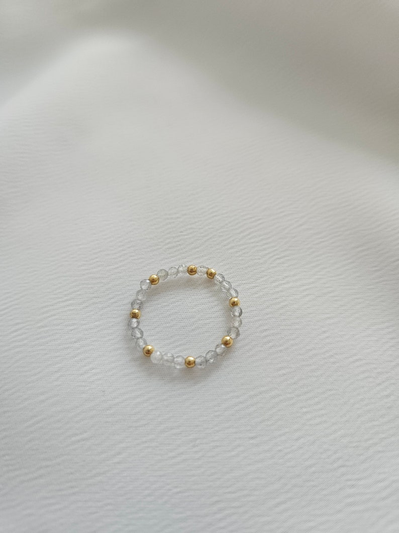 May include: A delicate bracelet made of clear and gold beads. The bracelet is made of small, round beads that are strung together on a thin, clear elastic cord.