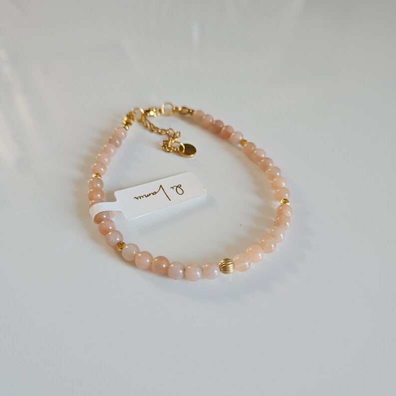 K&ouml;nnte beinhalten: Ein zartes goldenes Armband mit kleinen, hellrosa Perlen und goldenen Akzenten. Das Armband hat ein Etikett mit der Aufschrift "8 mm".