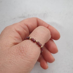 May include: A red gemstone ring with gold beads. The ring is on a person's finger.