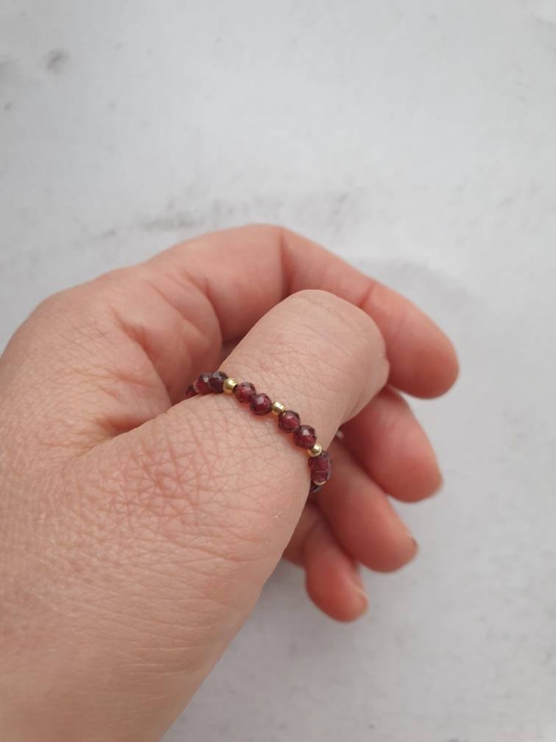 May include: A red gemstone ring with gold beads. The ring is on a person's finger.