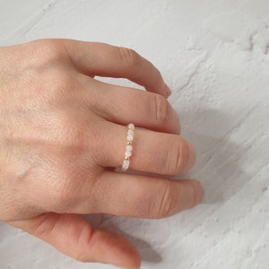 May include: A delicate ring made of small, pale pink beads strung on a gold wire.