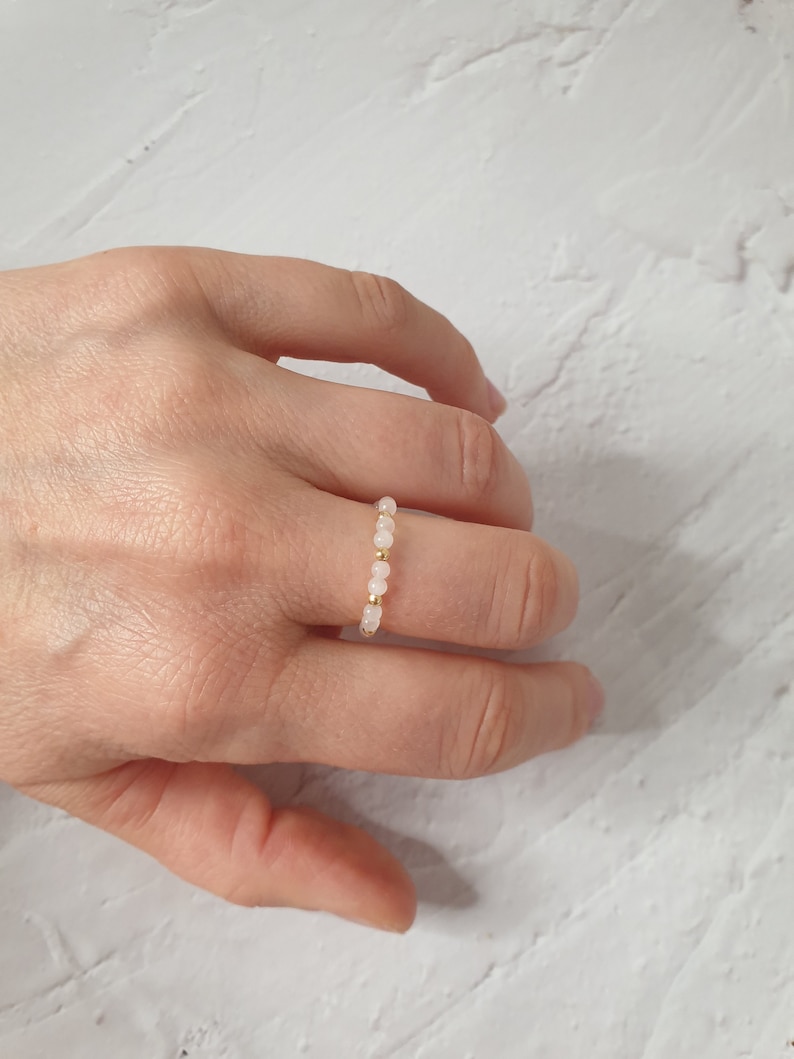 May include: A delicate ring made of small, pale pink beads strung on a gold wire.