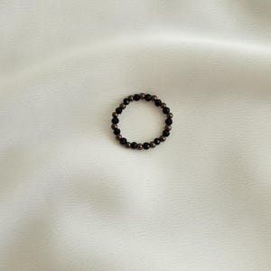 K&ouml;nnte beinhalten: Ein Ring aus schwarzen und goldenen Perlen. Der Ring besteht aus kleinen, runden Perlen, die auf einem d&uuml;nnen Draht aufgereiht sind.