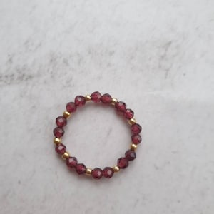May include: A red gemstone beaded ring with gold spacers. The ring is made with small, faceted beads and is a simple, elegant design.