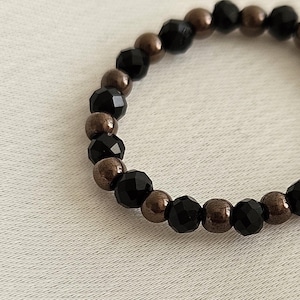 K&ouml;nnte beinhalten: Ein Armband aus schwarzen und bronzenen Perlen mit abwechselnd schwarzen facettierten Perlen und bronzenen Perlen.