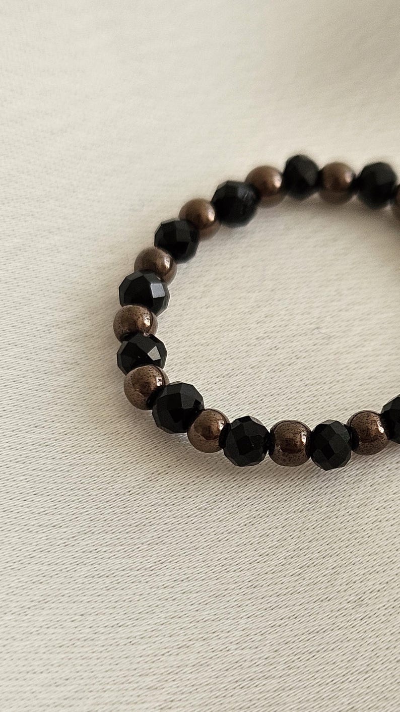 K&ouml;nnte beinhalten: Ein Armband aus schwarzen und bronzenen Perlen mit abwechselnd schwarzen facettierten Perlen und bronzenen Perlen.